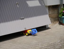 Spielzeug-LKW ist unter einem grauen Garagentor eingeklemmt